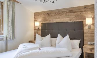A cozy bedroom with a wooden design and a large double bed. The decorative cushions and soft lighting create an inviting atmosphere.