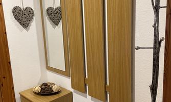 A modern entrance area with a wooden shelf, a mirror, and several coat hooks. Additionally, there are two round mats on the floor and a decorative bowl on the piece of furniture.