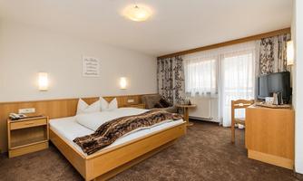 A cozy hotel room with a large bed and wood details. The windows are bright and let in a lot of light.