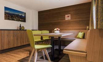 A cozy dining area with wooden details and modern green chairs. The walls are pleasantly painted in warm tones, and a picture is hung on the wall.