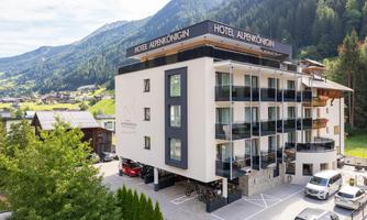 A modern hotel with the inscription "Hotel Auernig" in a green mountain landscape. The building features several balconies and offers a beautiful view of the surroundings.