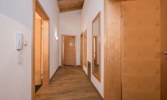 A bright hallway with wooden flooring and white walls. Doors and mirrors are arranged along the walls.