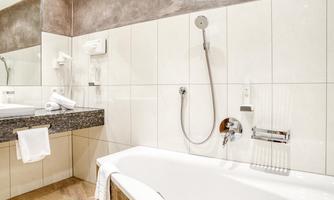 A modern bathroom with a bathtub and a shower. The walls are brightly tiled, and there is a large mirror above the sink.