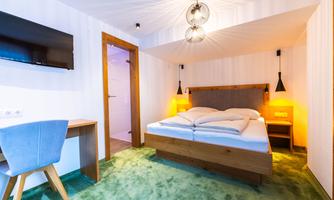 A modern hotel room with a comfortable double bed and a desk. The walls are bright and the lighting creates a cozy atmosphere.