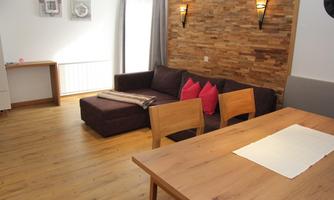 A cozy living room with a brown sofa and pink cushions. A wooden table with chairs complements the warm atmosphere of the room.