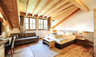 A cozy room with a wooden ceiling and large windows. It features a double bed, a seating area, and plenty of space.