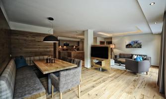 A modern living room with hardwood floors and a cozy seating area. The dining area consists of a large table and chairs, surrounded by warm wood tones.