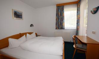 A simply furnished bedroom with a double bed and a desk. Bright curtains let in a lot of daylight.
