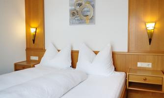 A cozy bedroom with two beds, decorated with white cushions. A modern artwork hangs on the wall, and there is warm lighting.