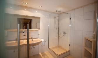 A modern bathroom with a glass shower and two sinks. The walls are covered with bright tiles, and there is plenty of light.