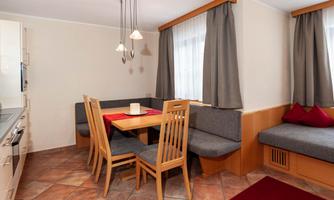 A modern kitchen with a dining area consists of a wooden table and several chairs. Gray curtains and a cozy seating area create an inviting atmosphere.