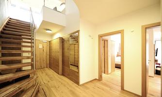 A modern entrance hall with a wooden staircase and bright walls. The floors are made of light wood, and there are several doors leading to adjacent rooms.
