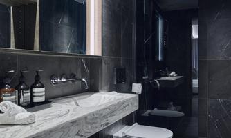 A modern bathroom with dark tiles and an elegant marble countertop. Towels and toiletries are neatly arranged on the table.