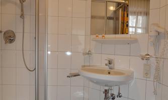 A modern bathroom with a shower cabin and a sink. The walls are tiled white, and the floor has a blue tile.