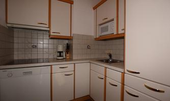 A modern kitchen with white cabinets and wooden accents. It is equipped with a dishwasher, a microwave, and a coffee machine.