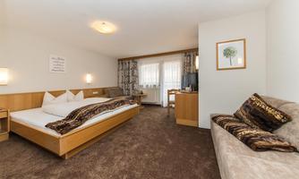 A modern hotel room with two beds and a cozy sofa. The warm colors and wooden details create an inviting atmosphere.