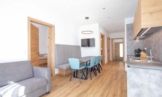 A modern living room with a cozy couch and a dining table. The walls are light and the floor is wooden, creating an inviting atmosphere.