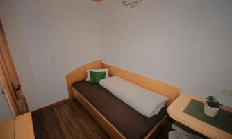 A simple room with a single bed and a small table. The walls are light, and there are decorations that create a cozy atmosphere.
