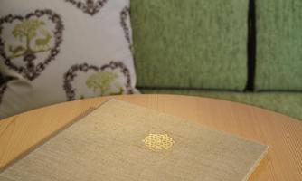 An elegant notebook lies on a wooden table. In the background, green cushions with a heart-shaped pattern are visible.