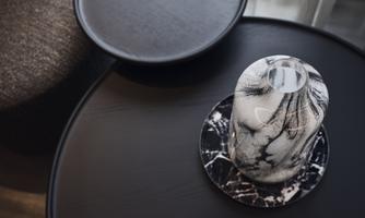 A stylish table with an elegant vase on a marbled coaster. The table has a modern, black surface and a simple shape.