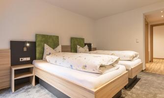 A modern bedroom with two beds and minimalist decor. The walls are light and the decoration is simple and fresh.