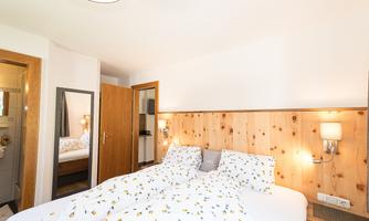A cozy bedroom with a double bed and wood paneling. The room is bright and inviting, with white bedding and a mirror.
