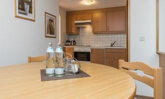 A bright kitchen with wooden cabinets and a round table. On the table are water droplets and a glass jug.
