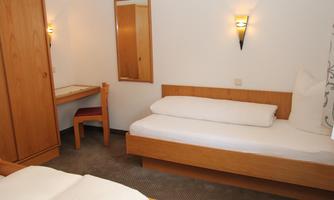 A simple room with two single beds and a desk. The walls are light and there is a mirror as well as soft lighting.