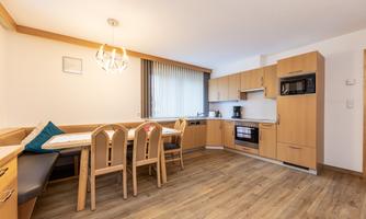 A modern kitchen with wooden cabinets and a cozy dining area. Bright windows create an inviting atmosphere.