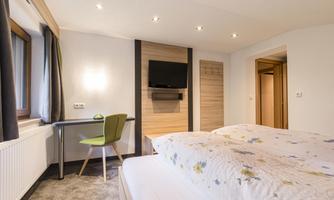 A modern bedroom with two beds and a television on the wall. A desk with a green chair complements the room.