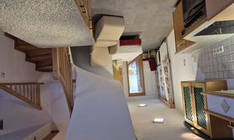 A modern apartment with an open kitchen and a comfortable armchair. Stairs lead to an upper area with a sleeping space.