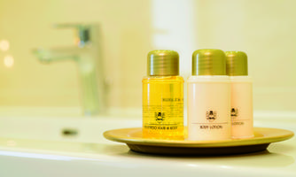Three care products in small bottles are placed on a plate. In the background, a modern faucet is visible.