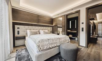 A modern bedroom with a large bed and elegant furnishings. Softly glowing ceiling lamps hang above the bed, and the room gives a cozy impression.