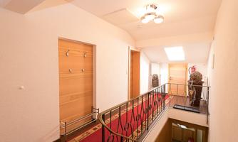 A bright hallway with a red carpet and modern wooden doors. Coat hooks are on the wall, and a staircase leads down.