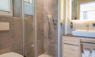 A modern bathroom with a glass shower and gray tiles. The wooden vanity features a stylish sink and reflects light well.