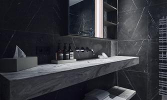 A modern bathroom with dark marble walls and an elegant sink design. Personal care products and towels are neatly arranged on the shelf.