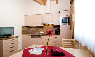 A modern kitchen with wooden furniture and a small seating area. A flower and some documents are on the table.