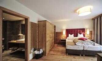 A modern hotel room with a comfortable bed and wood-paneled walls. Adjacent is a stylish bathroom with modern fixtures.