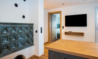 A modern room with a wood stove and a television on the wall. The floor is made of wood, and there is an entrance to another room.