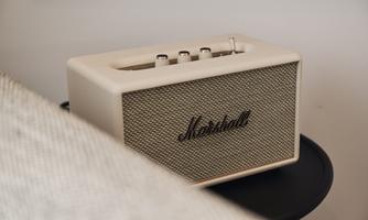 An elegant speaker from the brand Marshall in a stylish beige color. It features rotary knobs and sits on a dark-toned table.