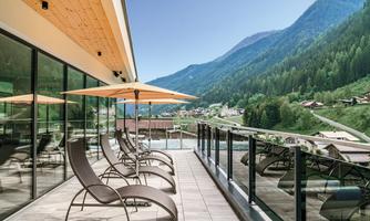 A modern terrace with lounge chairs and sun umbrellas. In the background, green mountains and a picturesque landscape stretch out.