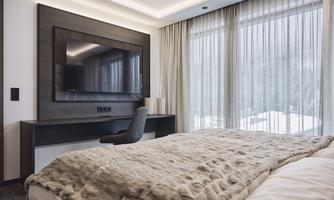A modern bedroom with a large bed and a television on the wall. Large window area with curtains that offers a view of the snowy landscape.
