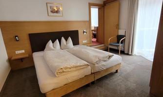 A cozy hotel room with two beds and comfortable pillows. The room has large windows and a chair in the corner.