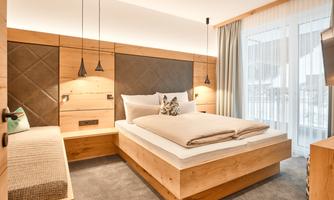 A modern bedroom with wooden details and a cozy bed. Large windows provide plenty of daylight.