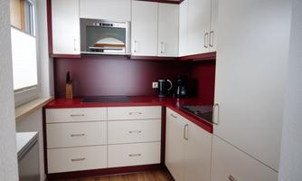 A modern kitchen with white cabinets and a burgundy backsplash. It features a stove, a microwave, and a coffee maker.