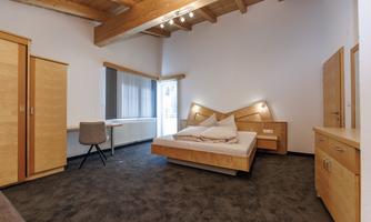 A modern bedroom with a double bed and wooden interior. Large windows provide plenty of natural light.