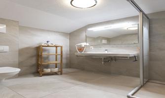 A modern bathroom with a large mirror wall and an elegant shower. There is a wooden shelf with toiletries.