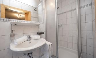 A modern bathroom with a shower and a sink. The walls are tiled and there is a reflective surface.