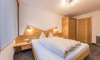A modern bedroom with a double bed and wooden details. There is a wardrobe and a gentle, warm glow of light.