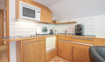 A modern kitchen with wooden cabinets and white tiles. The equipment includes a microwave, an oven, and a coffee maker.
